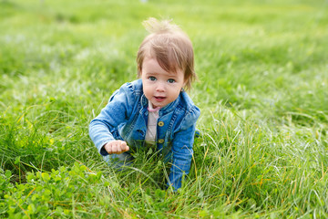 Baby girl crawling on the green grass outdoors in summer