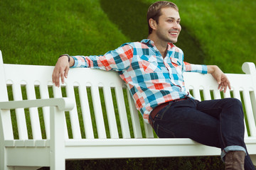 Portrait of happy young happy man relaxing near green lawn in park