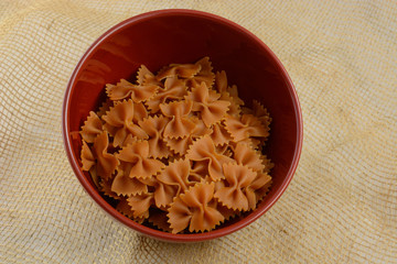 Dry uncooked Carrot and squash vegetable farfalle bow tie pasta in red bowl 