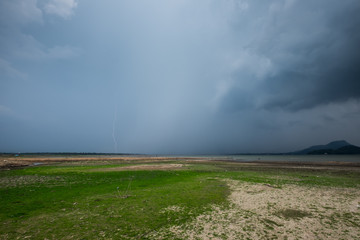 Grass land with storm rain cloud and lightning bolt over the lake.