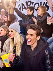 Sport fans loud shouting on tribunes. Large group people on tribunes cheer on team. Sport fans eating popcorn.