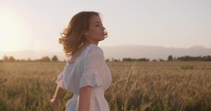 Beautiful girl running on sunlit wheat field. Slow motion 240 fps. Sun lens flare. Freedom concept. Happy woman having fun outdoors in a wheat field on sunset or sunrise.Harvest