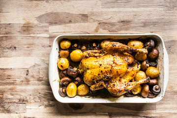 roasted curry chicken with potatoes and mushrooms in a plate on an old oak table seen from above
