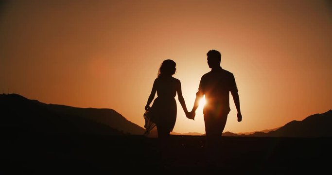 couple silhouette walking in the highlands holding hands with the sunset Golden hour, the sun a warm color, slow motion