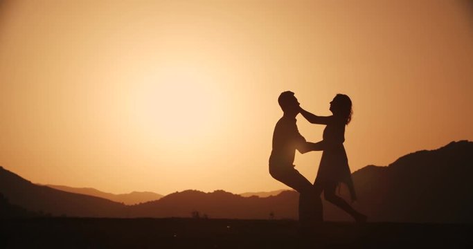 Romantic young couple silhouette. Woman running to her man and they hug and spin at sunset Golden hour, slow motion