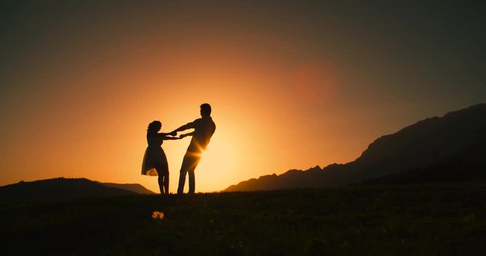 Romantic young couple silhouette. woman and man holding hand in circle together,dawn, the glare of the sun, love story, slow motion