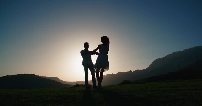 Romantic young couple silhouette. woman and man holding hand in circle together,dawn, the glare of the sun, love story, slow motion