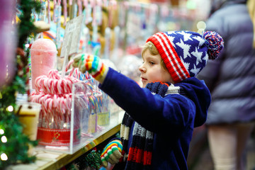Little kid boy with candy cane stand on Christmas market