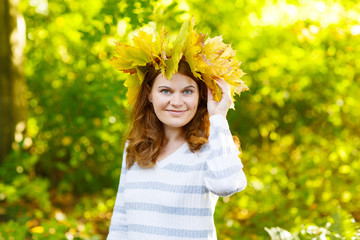 Happy young woman with autumn maple leaves garland in park.