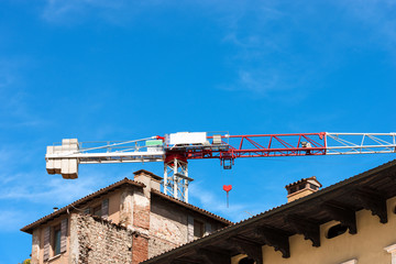 Construction site with a red and white crane and old house on a clear blue sky