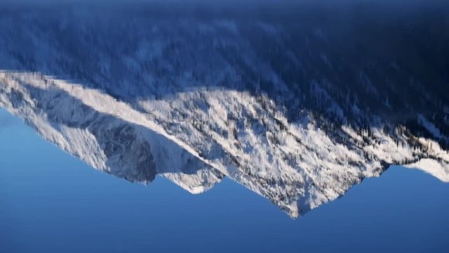 Reflection of mountain peaks in water of Lower Multinskoe lake in the Altai Mountains on blue sky background.