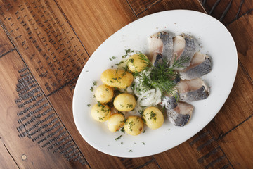 Herring fish with young potato on white plate. wooden background.