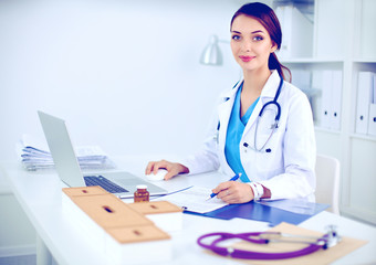 Fototapeta premium Beautiful young smiling female doctor sitting at the desk and writing.