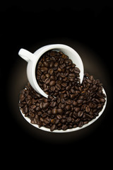 Mug of coffee beans with saucer on black and yellow background.