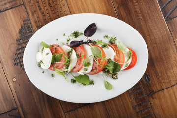 Salad with Mozzarella cheese and tomatoes in white oval plate. wooden background.
