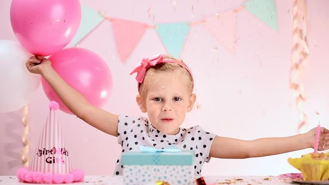 Cute birthday girl with colorful balloons and falling confetti playing in decorated room. Concept of event celebration and lifestyle.  