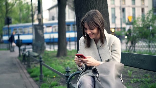 Young woman using smartphone sitting on bench in city park
