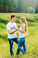 A nice couple in a forest area standing together looking at each other gently, wildflower bouquet in their hands. Boyfriend gives his girl flowers