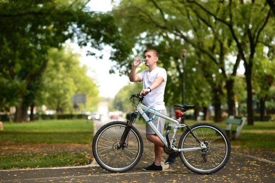 Young blond man on bicycle stoping to drink water