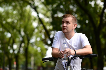 Young blond man on bicycle stoping to drink water