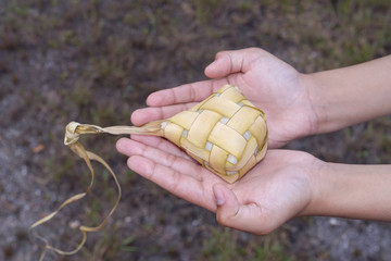 A hand holding Ketupat (Rice Dumpling) - Malay cuisine made from glutinous rice packed inside a diamond shaped container of wooven palm leaf.