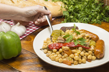 comida española, potaje de garbanzos con con carne chorizo y morcilla, una mano metiendo la cuchara en el plato