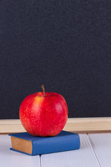 Red apple on old mini book against blackboard
