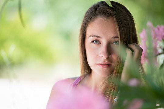 Beautyful lady in a headshot, very clean skin and beautiful features. Green leafs and pink flowers as background