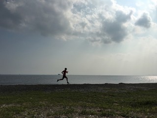 Silhouette of man running on stony pebble beach by sea