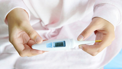 Close-up of Asian girl hand holding electronic body thermometer displaying very high temperature 39 C, health and illness concept