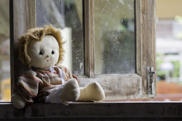 Doll girl sitting by the window alone .