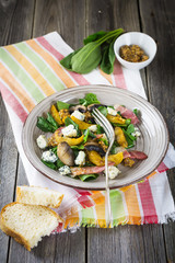 Warm autumn salad with potatoes, mushrooms, bacon, spinach, mustard sauce and cheese on orange napkin. Wooden old background. Selective focus.