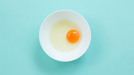 Top view of raw egg in white bowl on blue background.
