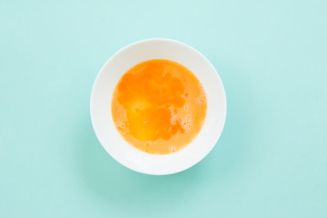 Beat egg in white bolw on blue background.