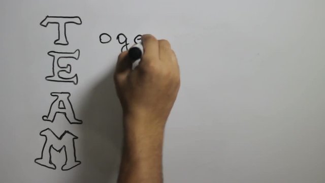 Hand writing a "Team" message on a white board using a black marker