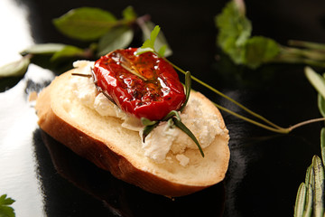 Slice of dried tomato on bread piece on black background