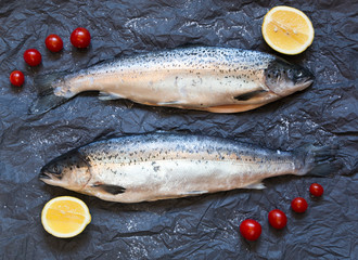 Fresh uncooked fish on black background with tomatoes, lemon, to