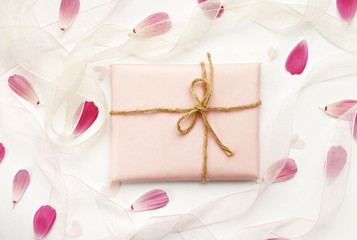 handiwork gift wrapped in pink paper with twine bow, arranged amidst flower petals and ribbons. Dreamy soft congratulation background.  