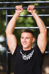 Naklejka premium Young man doing pull ups on horizontal bar outdoors, workout, sport concept