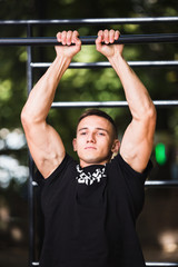 Young man doing pull ups on horizontal bar outdoors, workout, sport concept