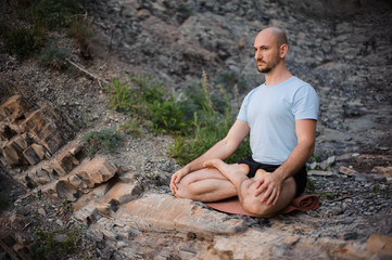 Man meditating in the mountain in the morning. Doing yoga outdoors on the cliff.