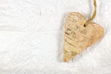 Wooden heart on white handmade crumple paper. Love and valentine's day concept.