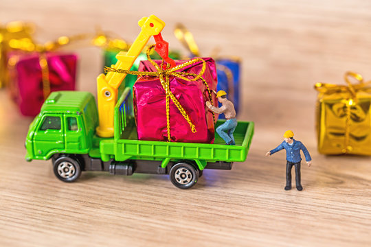 Miniature Worker Passenger Gift Box by Truck on Wooden floor ,Determined Image for Christmas Holiday and Happy New Year Gift Celebration concept.
