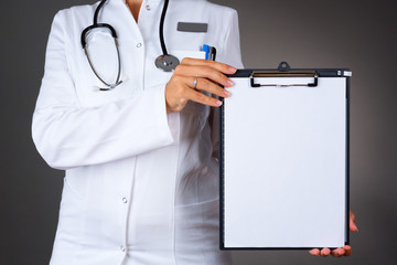 Close up of a woman doctor, holding a blank paper, isolated on dark background.