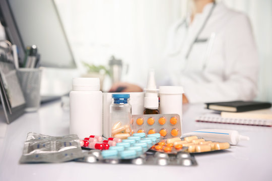 Various colorful medicines on top of the table, with female doctor working on the desk in the background.