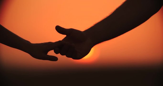 4k,Close up of the hands of a romantic couple holding hands at sunset silhouetted, slow motion