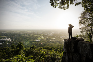 Man traveler is talking on the phone on cliff with beautiful landscape sunset - obrazy, fototapety, plakaty
