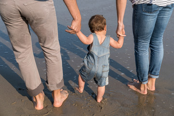 10 month old baby boy walks with mom and dad on the beach - obrazy, fototapety, plakaty