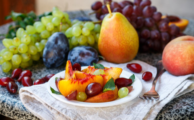 Fruit salad in white plate. Snack of fresh peaches, grapes, dogwood, plums, and mint leaves. Healthy Breakfast. Selective focus
