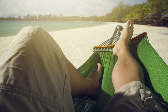 Man relaxing in the hammock set on the beach,flare light